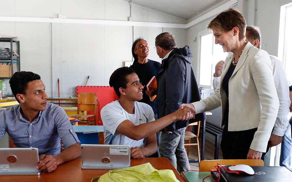 La conseillère fédérale Simonetta Sommaruga salue deux jeunes réfugiés dans une salle de cours du camp de réfugiés de Moria