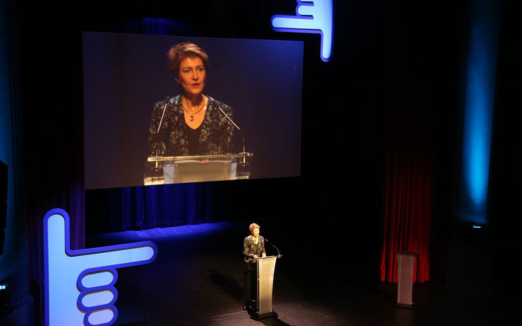 La conseillère fédérale Simonetta Sommaruga est sur l’estrade au pupitre de l’orateur et parle. Son image est diffusée sur un grand écran derrière elle.