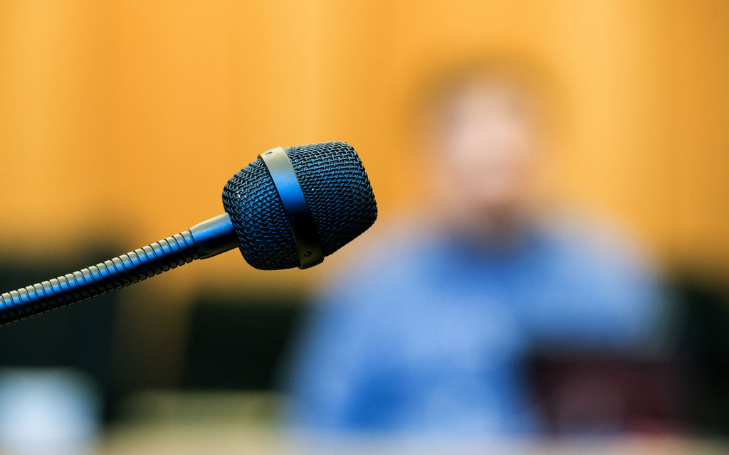 Immagine sfuocata di un testimone dietro al microfono in una sala di tribunale