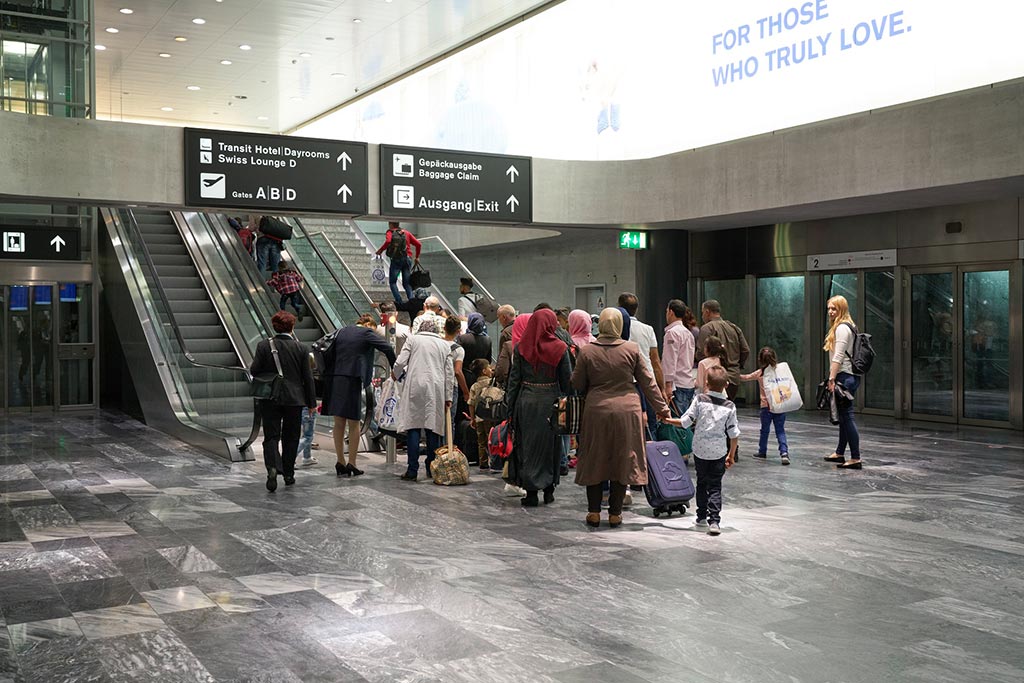 Frauen mit Kopftüchern, Kinder und Männer stehen vor einer Rolltreppe im Flughafen Zürich.